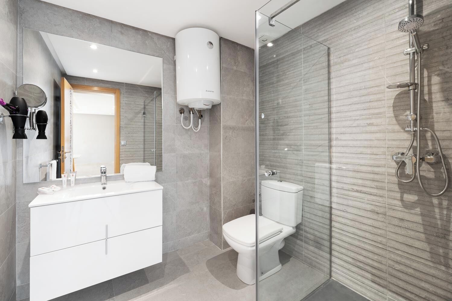 Un baño moderno con cabina de ducha de vidrio, inodoro blanco y tocador con espejo.