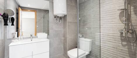 Un baño moderno con cabina de ducha de vidrio, inodoro blanco y tocador con espejo.