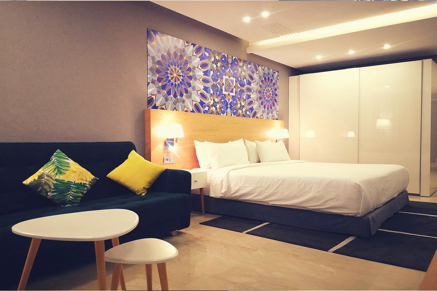 A hotel room with a bed, a sofa, a small table, and a wall art piece.