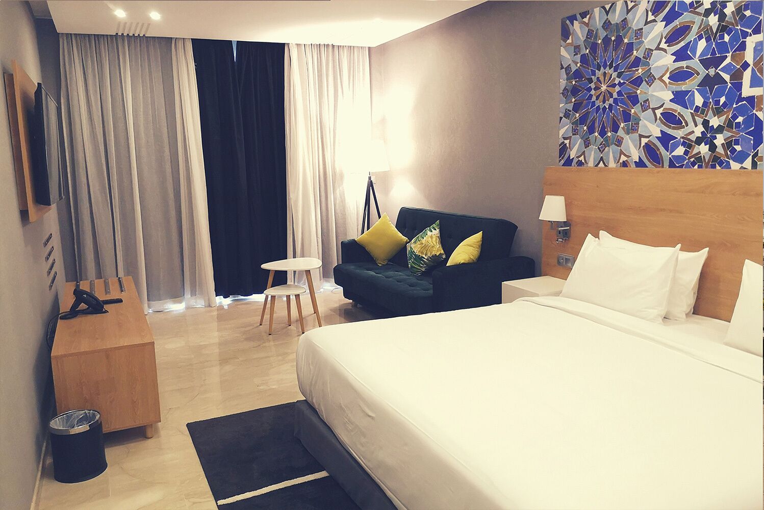 Una habitación de hotel con cama, sofá, una mesita y televisor sobre un soporte de madera.