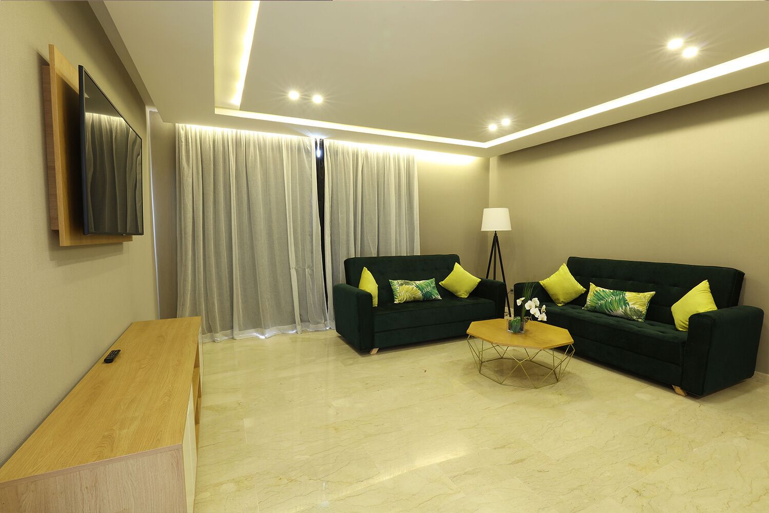 A modern living room with two dark green sofas, a wooden coffee table, and a TV mounted on the wall.
