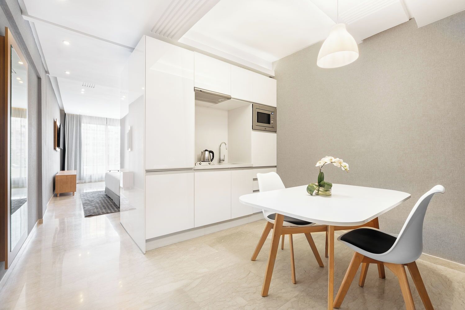 A modern kitchen with white cabinets, a stainless steel microwave, and a kettle on the counter.