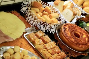 Diversos produtos de panificação, incluindo pão, doces e um bolo, sobre uma mesa.