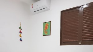 Una habitación con dos camas individuales, un mueble blanco pequeño, aire acondicionado instalado en la pared y una ventana con persianas marrones.