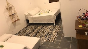 Una habitación de hotel pequeña con dos camas, un adorno de pared tejido, un televisor pequeño y una cesta de aperitivos en la cómoda.