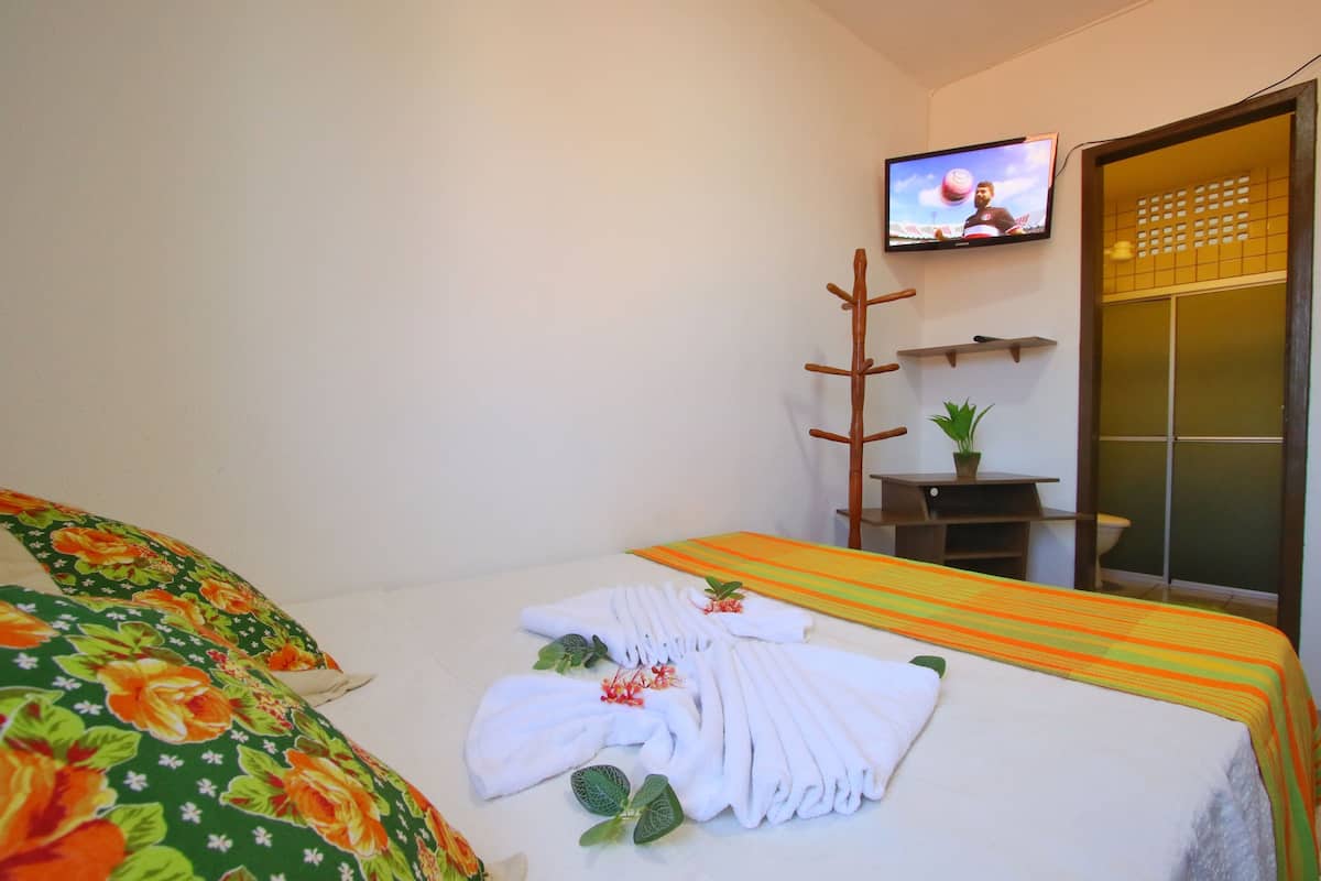 A hotel room with a neatly made bed, a television on the wall, and a small table with a plant.