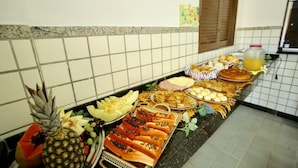 Un bufé con diversas opciones de comida, incluyendo frutas, pasteles y un recipiente para bebidas.