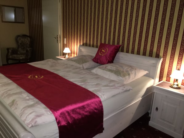 A neatly made bed with a red blanket and pillows, a bedside lamp, and a chair in a hotel room.