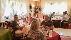Un groupe de personnes est assis à une table dans une pièce ornée d’un lustre et d’une horloge murale.