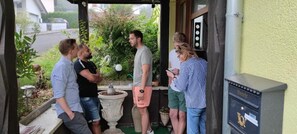 Un groupe de personnes se tient devant un bâtiment, près d’une boîte aux lettres et d’un pot de fleurs.