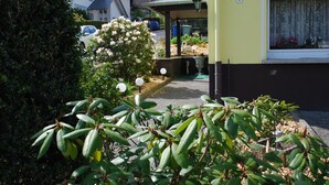 Un quartier résidentiel avec un immeuble jaune, une voiture blanche garée à proximité et un jardin agrémenté de diverses plantes et fleurs.