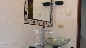 Et badeværelse med en vask i glas, et hvidt toilet og et spejl med dekorativ ramme.