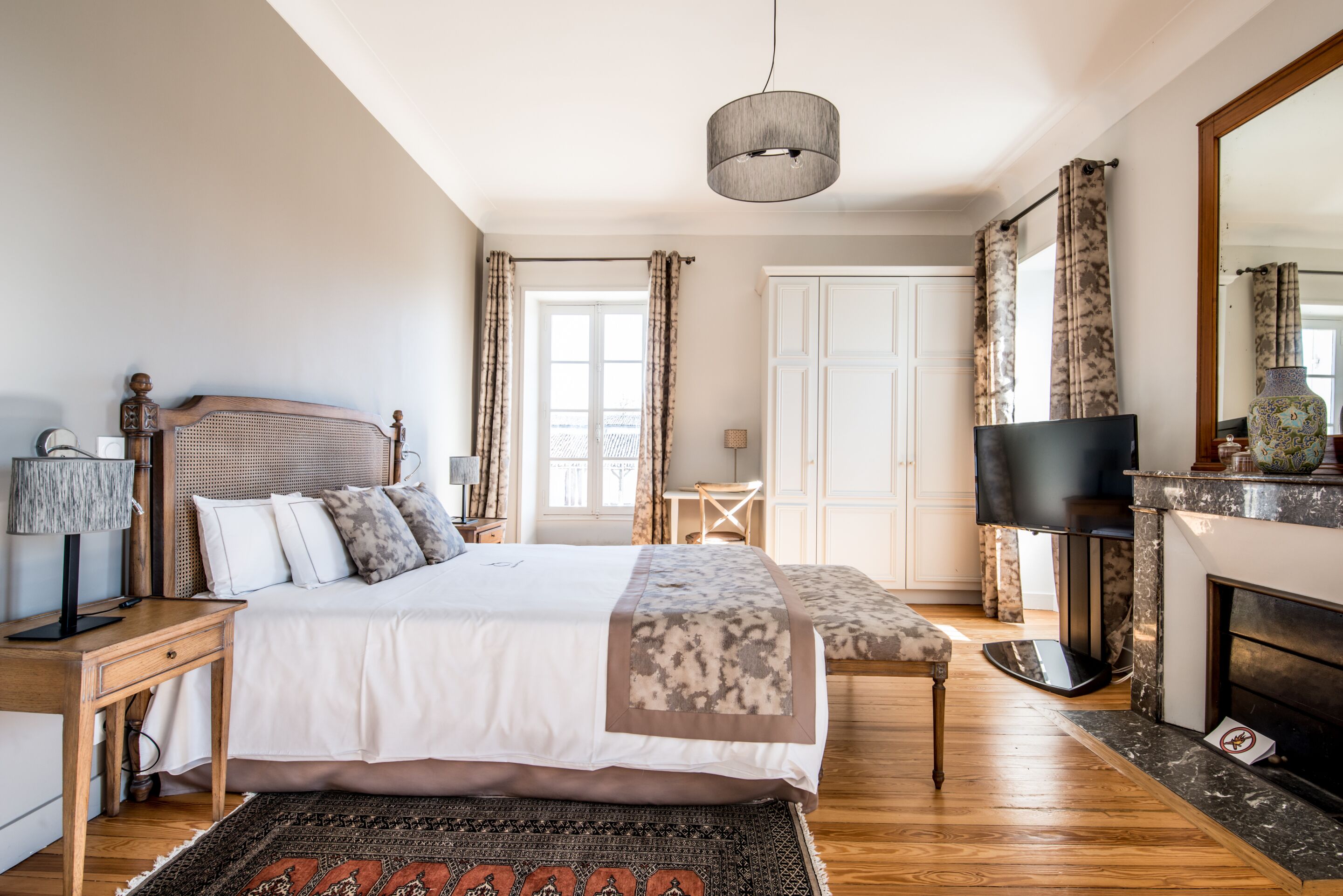 Ein Schlafzimmer mit Bett, Nachttisch, Lampe, Fernseher, Kamin und Blick ins Freie.