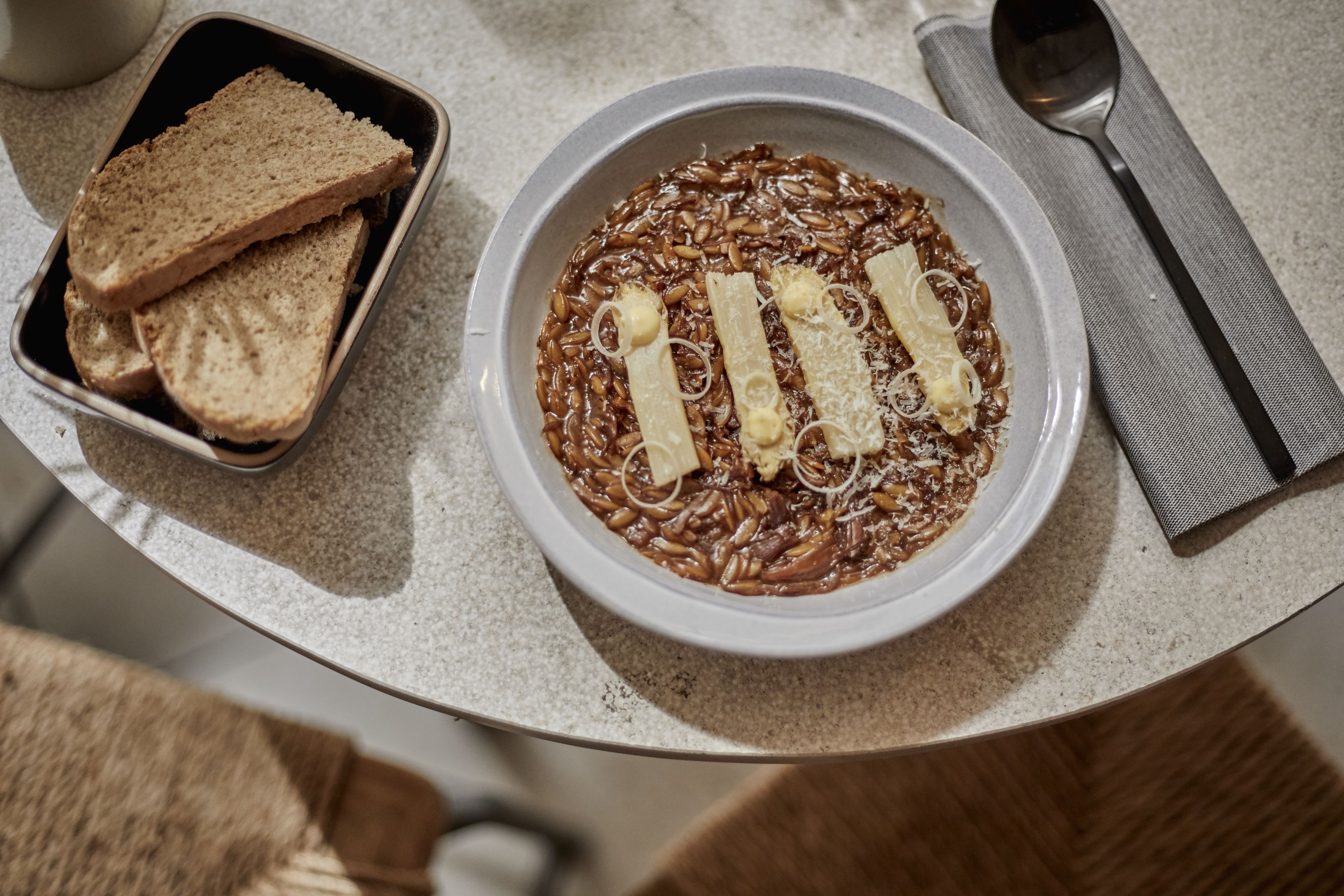 A bowl of noodles with strips of cheese and a plate of bread on a table.