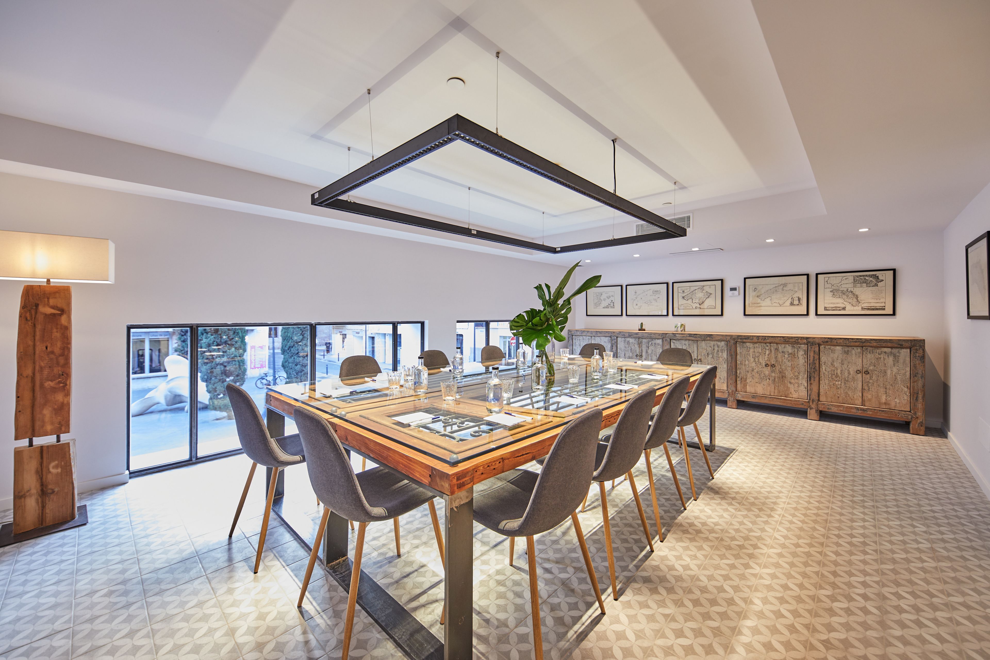 Un comedor espacioso con una gran mesa de madera, sillas modernas y una mesa con cubierta de vidrio. Se observan obras de arte enmarcadas en las paredes y un aparador de madera al fondo.