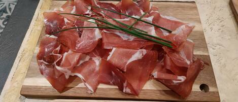 Una tabla de madera con jamón serrano en lonchas y cebollines sobre un suelo de baldosas.