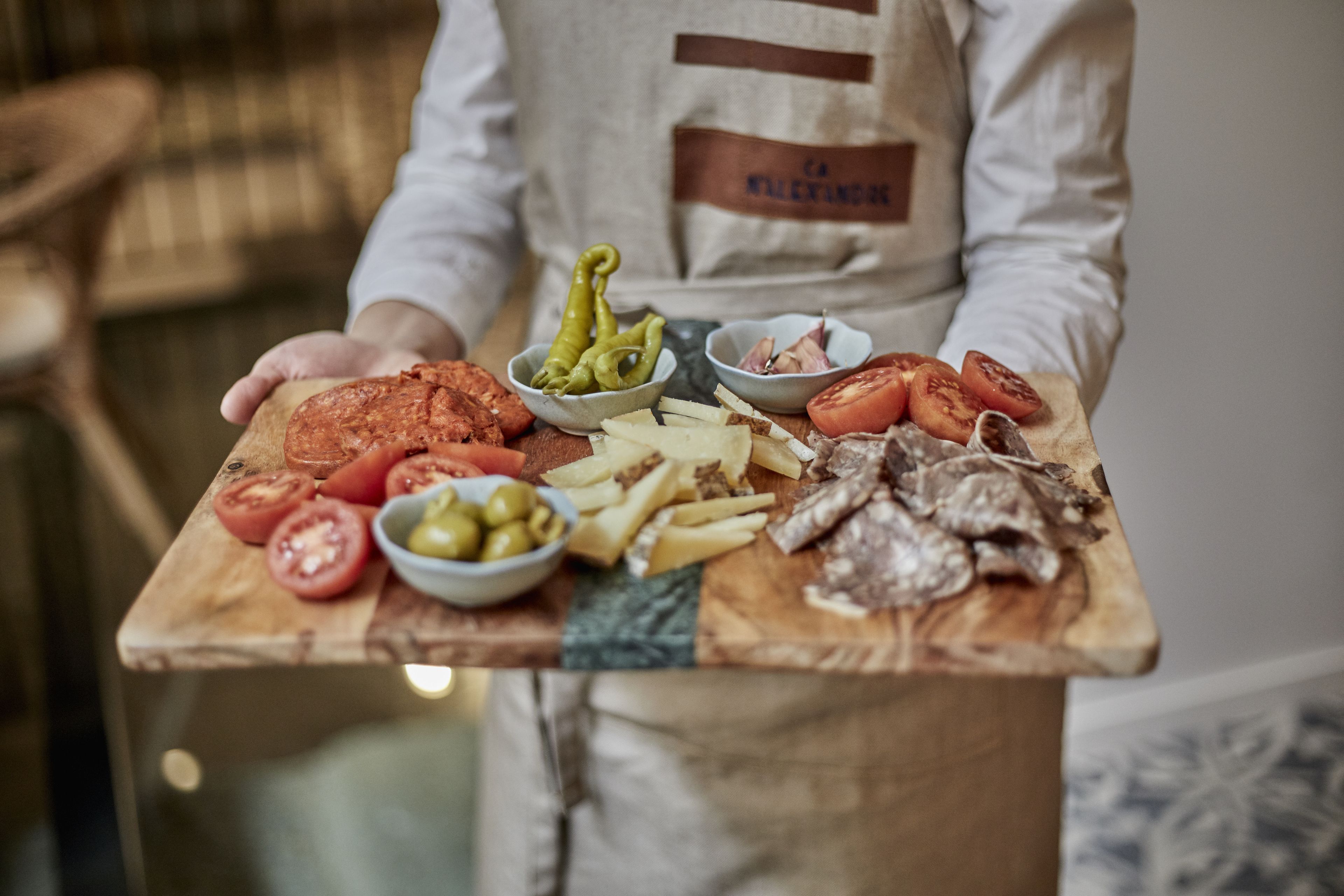 A wooden cutting board with various food items including tomatoes, olives, cheese, and meat.