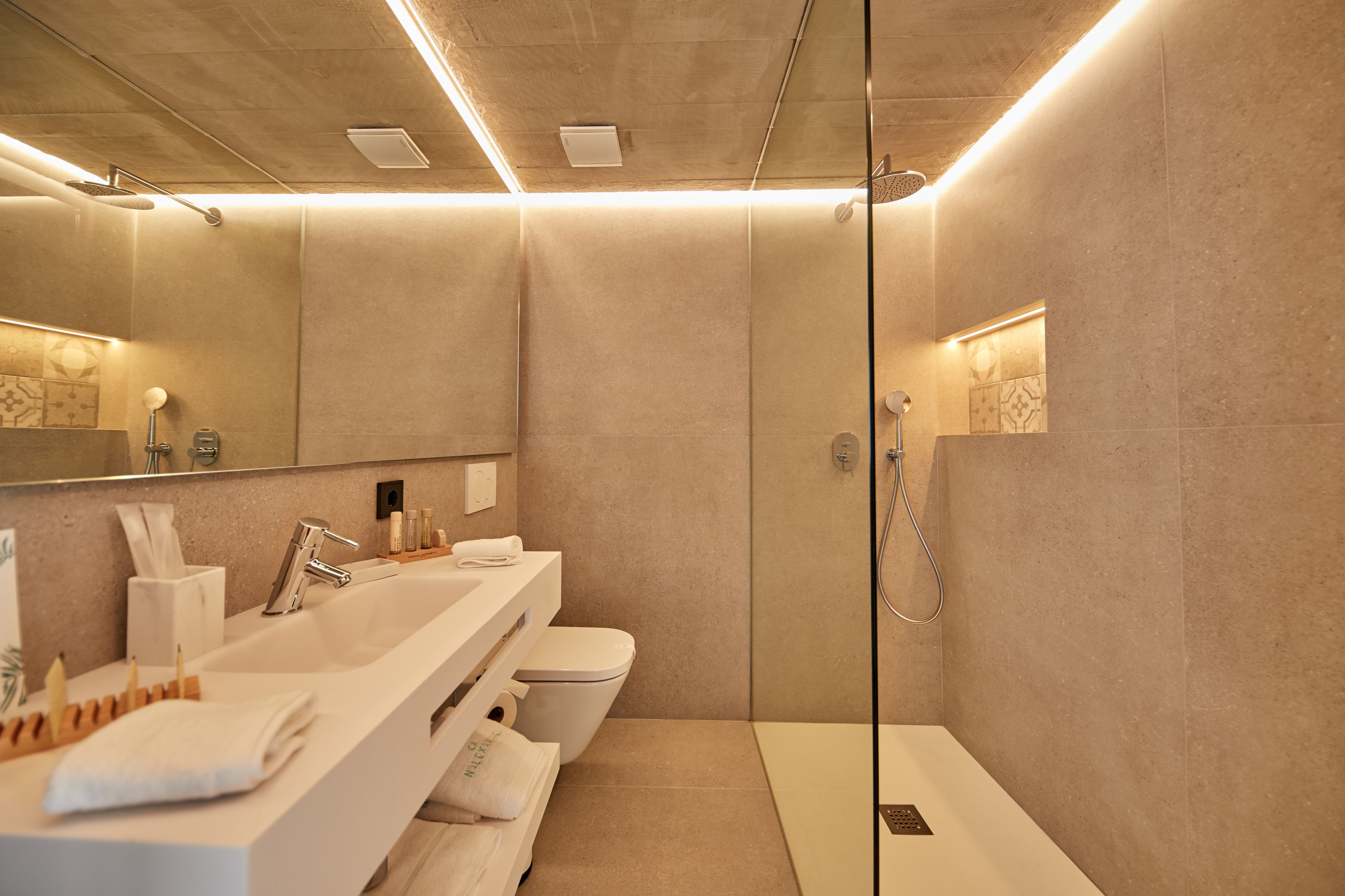 A modern bathroom with a large mirror, a white sink, a toilet, and a shower area.