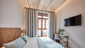 Ein Schlafzimmer mit Bett, Schreibtisch, Stuhl, Fernseher und einem Fenster mit Vorhängen.