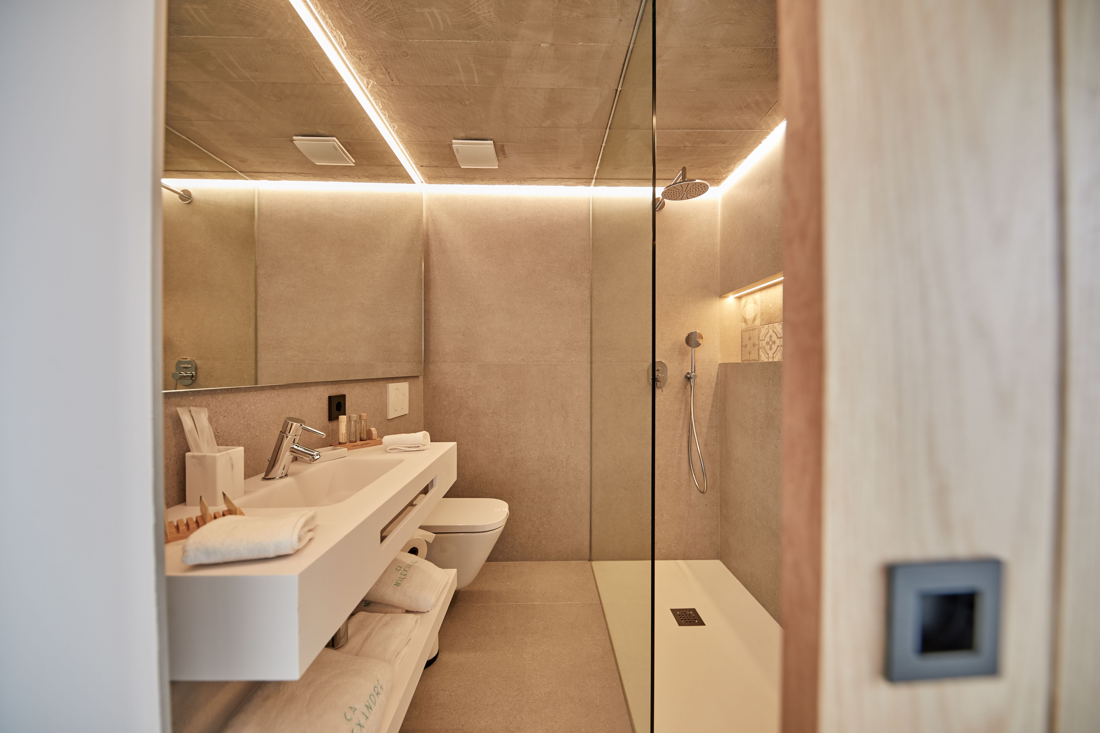 Un baño moderno con mampara de vidrio, un lavamanos blanco, un inodoro y zona de ducha.