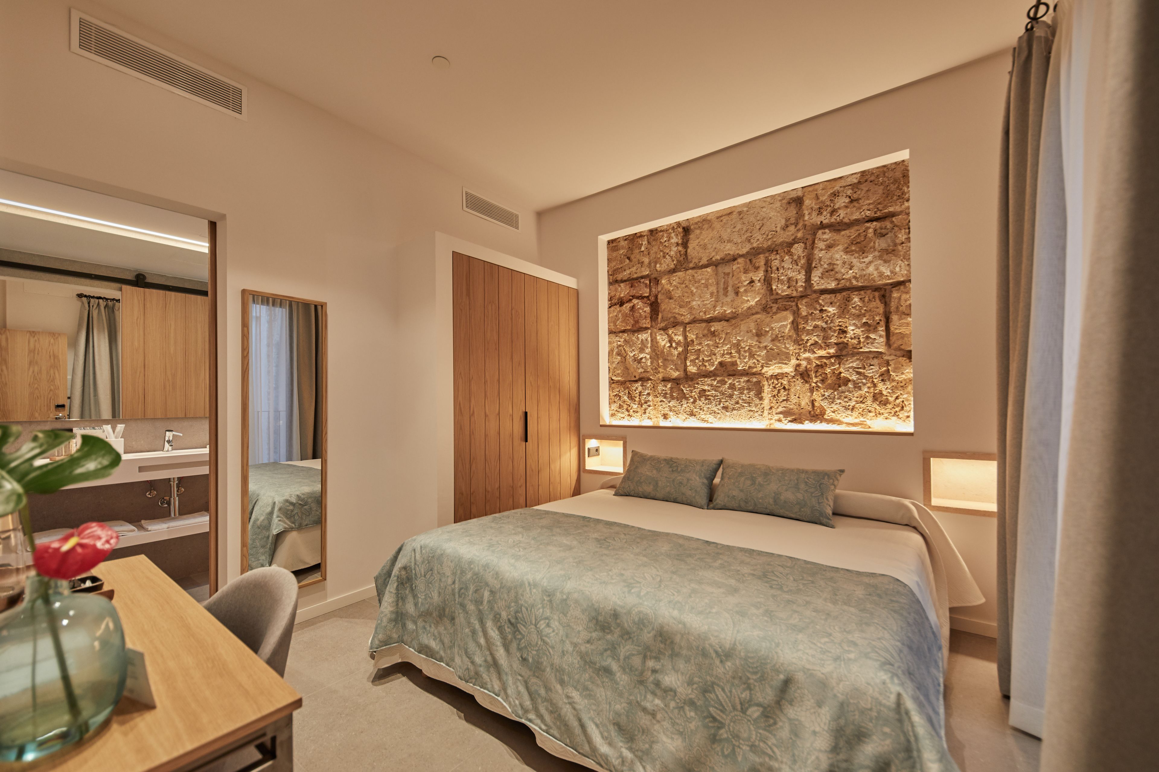 A modern hotel room with a large bed, a wooden wardrobe, a desk with a vase, and a large wall mural.
