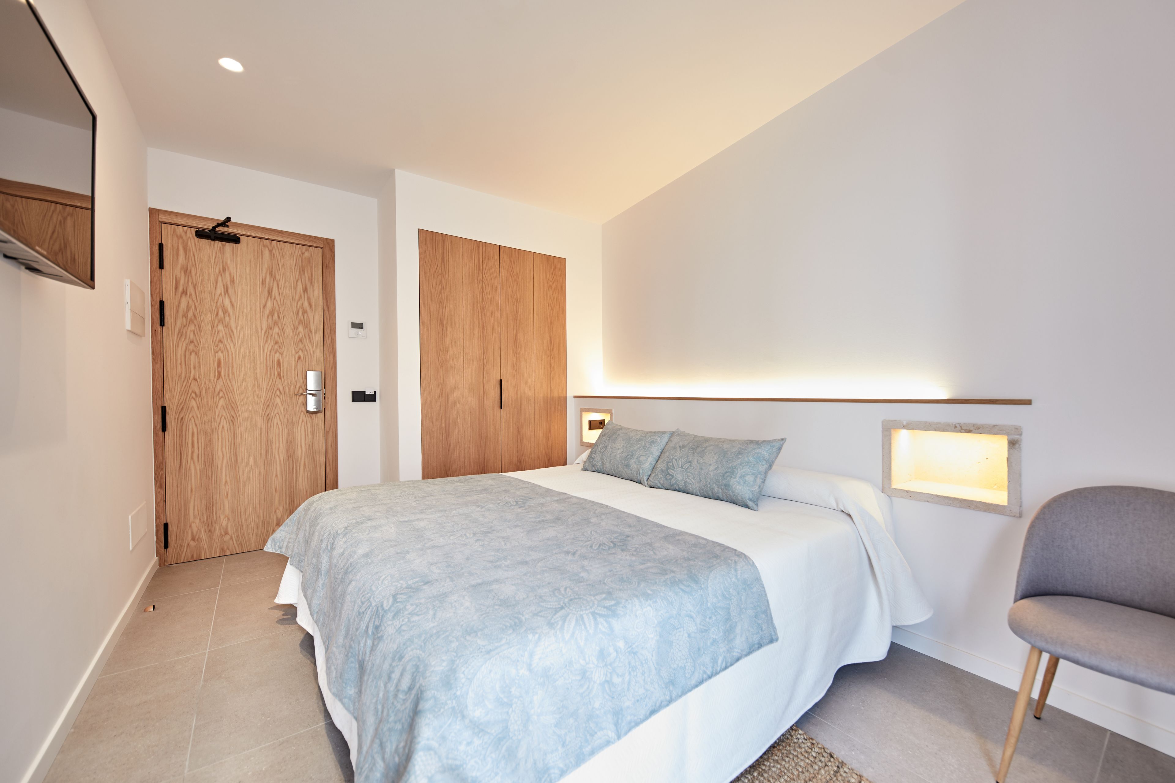 Un dormitorio moderno con una cama grande, un armario de madera, una mesita de noche y una silla.
