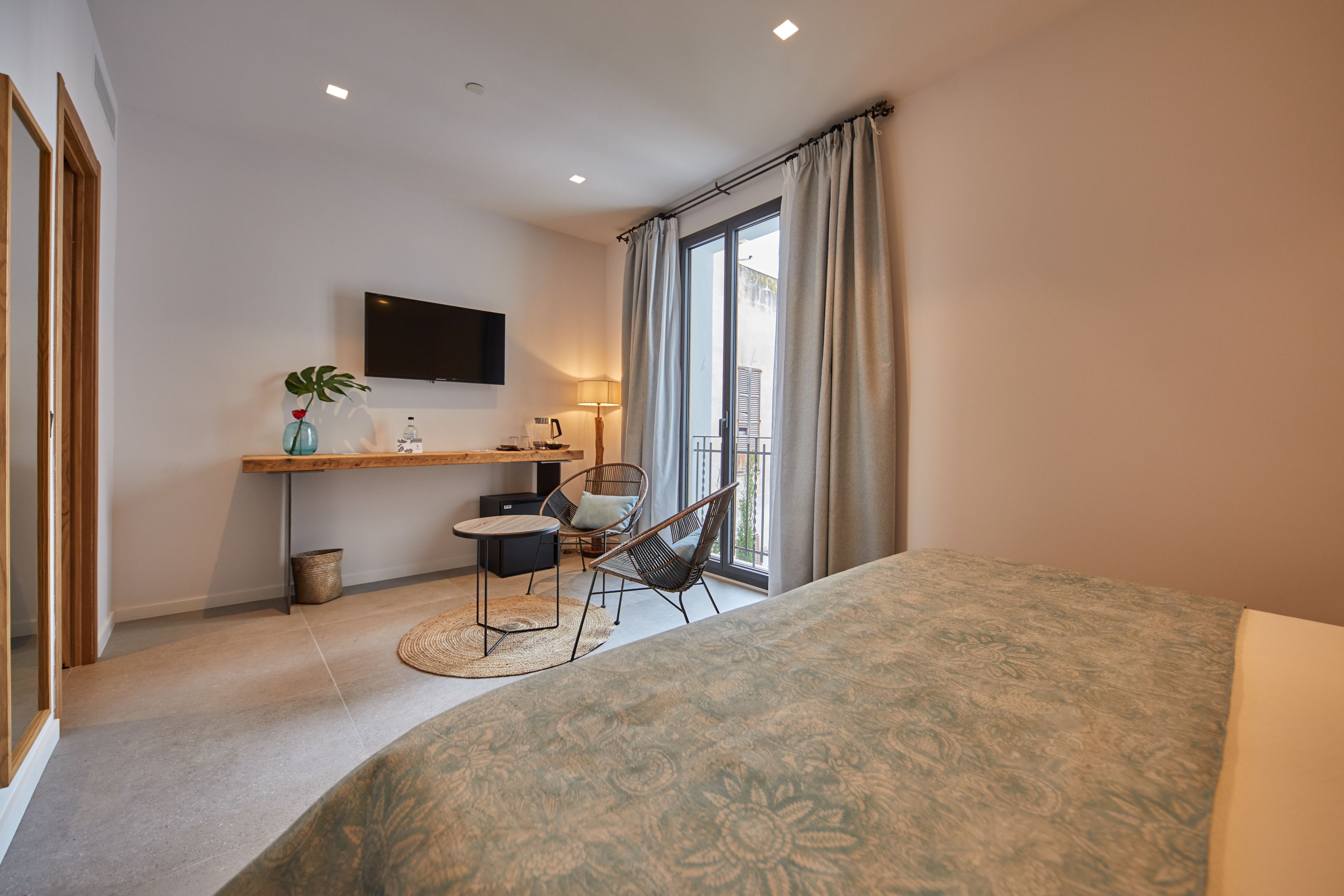 A modern bedroom with a large bed, a desk with a chair, a TV, and a balcony with curtains.
