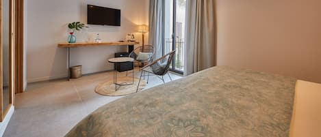 Et moderne soveværelse med en stor seng, et skrivebord med stol, et fjernsyn og en balkon med gardiner.