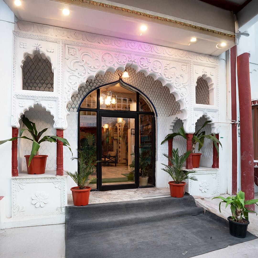 A building entrance with ornate white and red architectural details, a black glass door, and potted plants on either side.