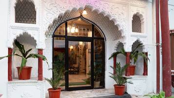 A building entrance with ornate white and red architectural details, a black glass door, and potted plants on either side.