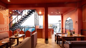 Restaurante com escadaria que leva a um balcão, mesas e vista para a cidade.