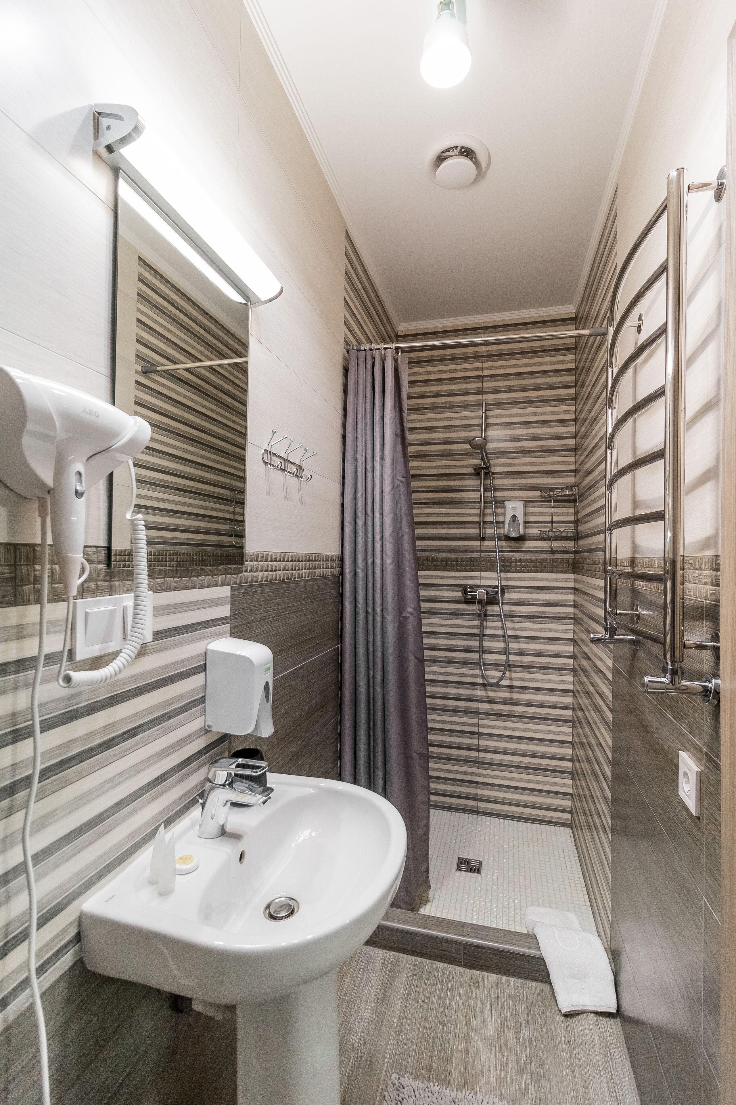 A modern bathroom with a sink, mirror, hairdryer, and shower.