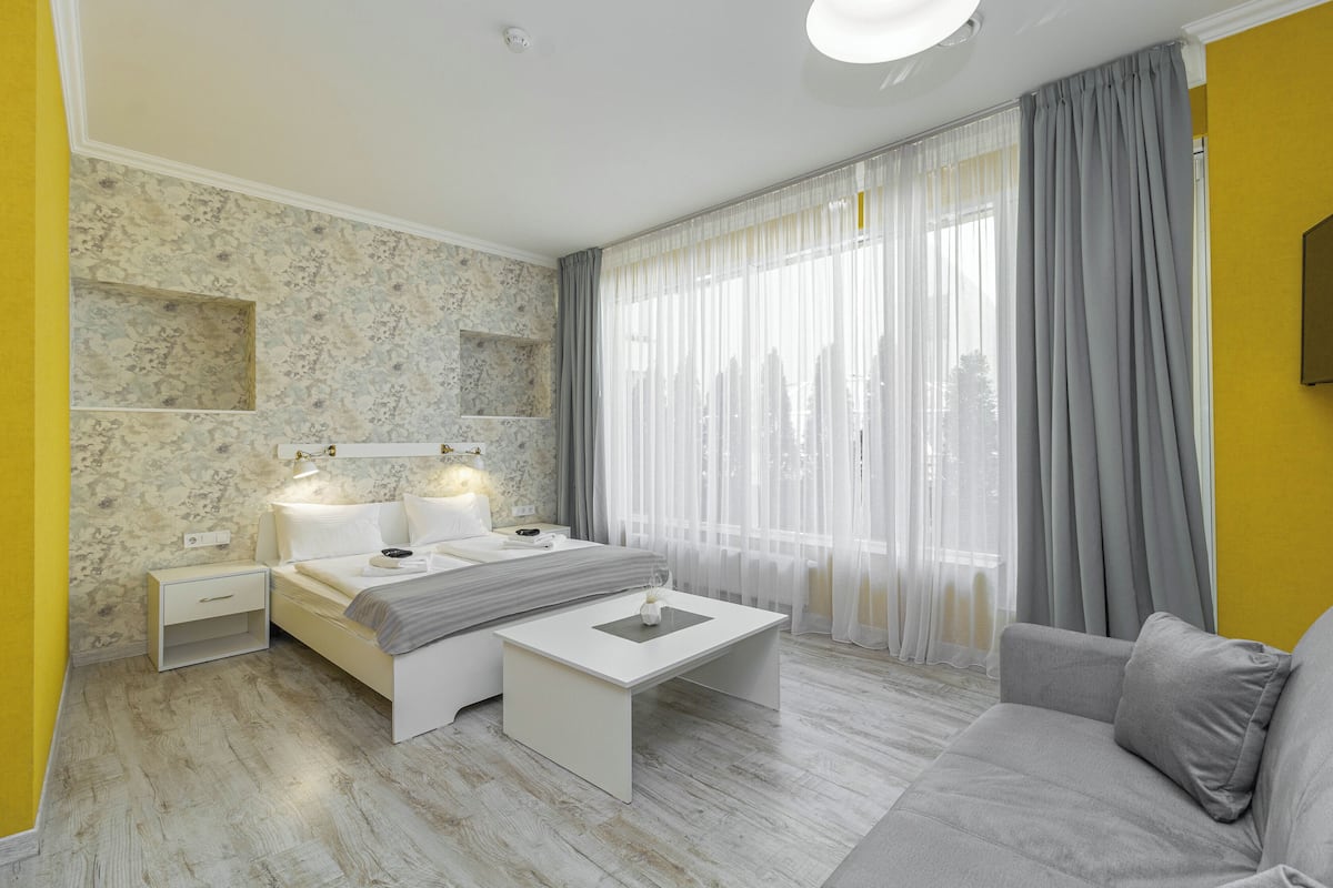 A modern bedroom with a bed, bedside tables, a nightstand, a sofa, and a window with curtains.