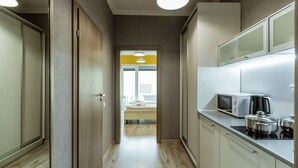 Un pasillo estrecho con un área de cocina a la derecha, que incluye armarios, un microondas y una estufa.