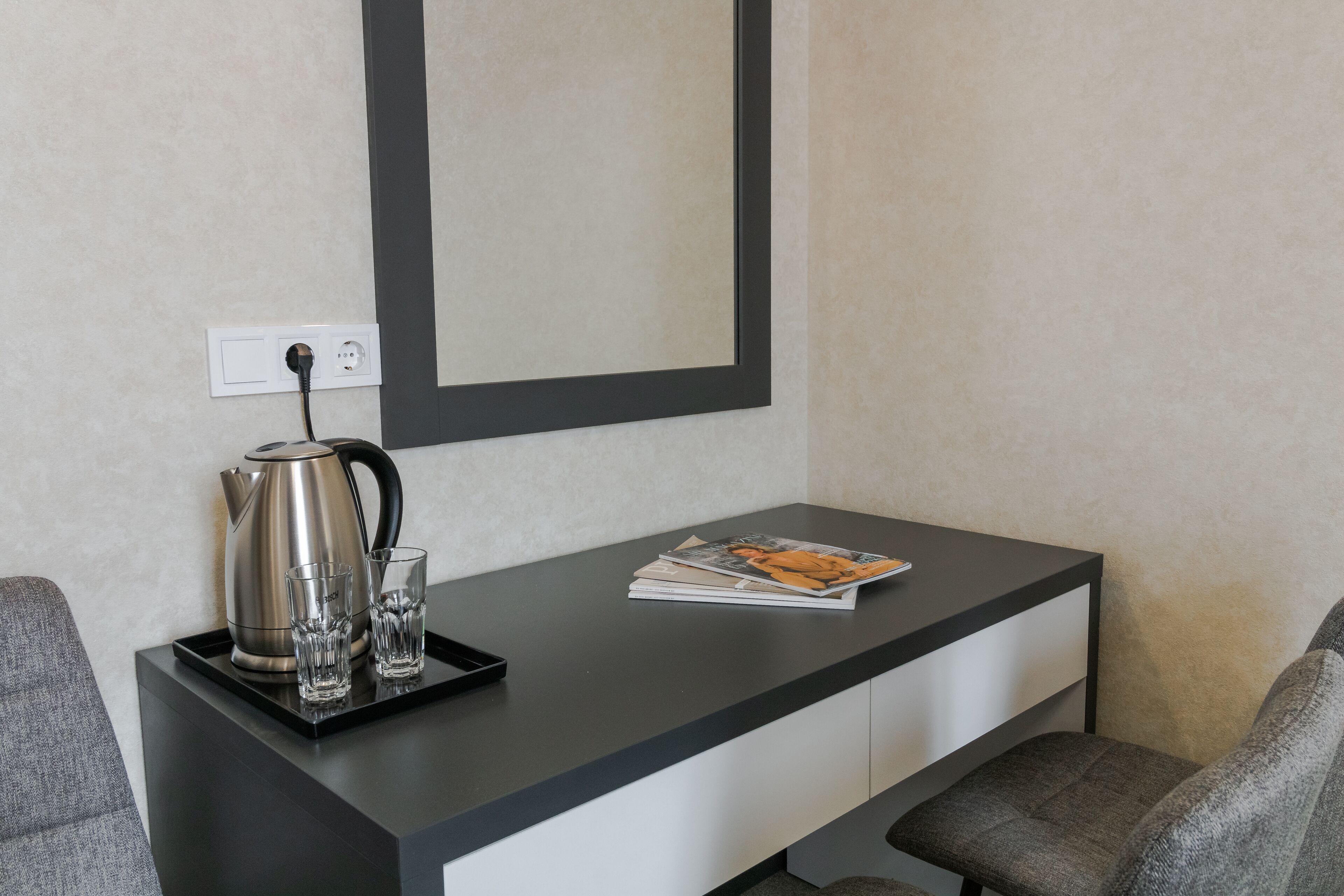 Una habitación de hotel moderna con un escritorio negro, una tetera, dos vasos y una revista.