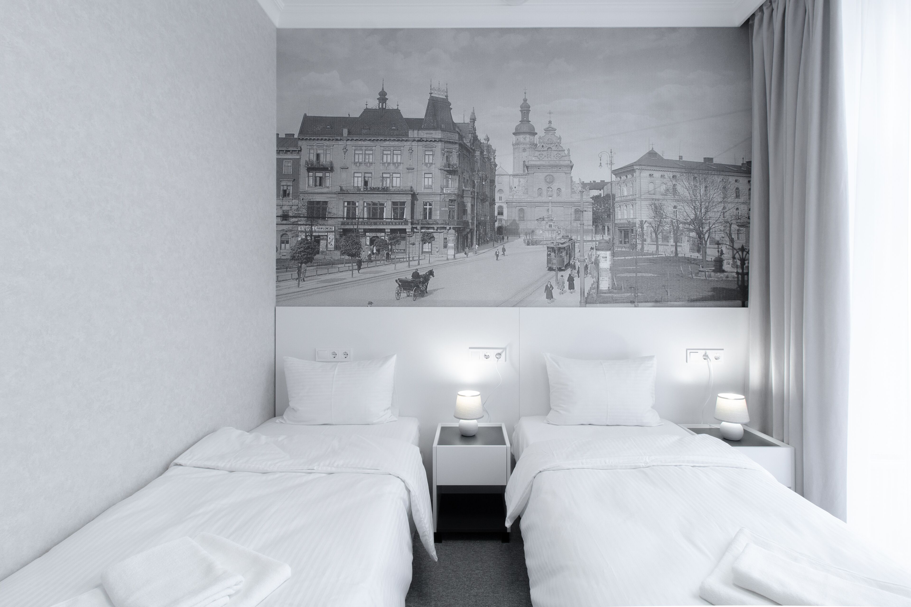 A hotel room with two beds, a cityscape mural on the wall, and a view of the street outside.