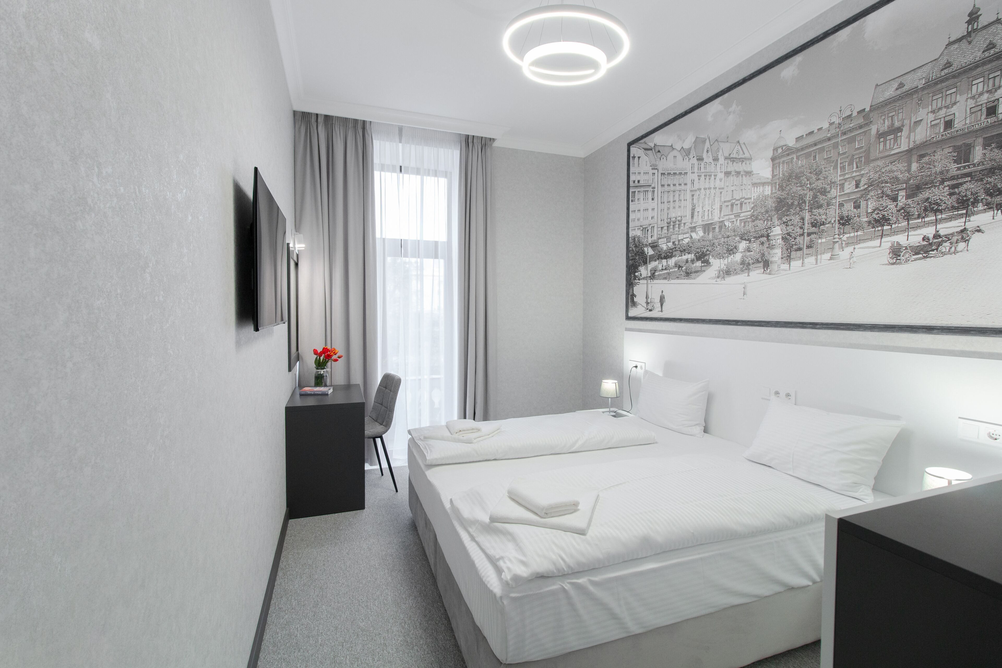 Habitación de hotel moderna con dos camas, un escritorio, una silla, un televisor de pantalla plana y una fotografía grande enmarco de un paisaje urbano.