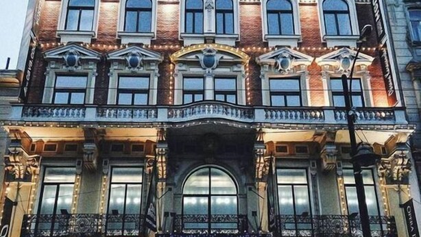 Un edificio histórico con arquitectura ornamentada, que cuenta con un balcón central y varias tiendas a nivel de calle.