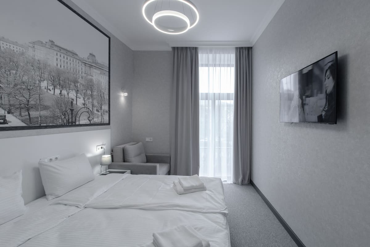A modern hotel room with a large bed, a seating area, a flat-screen TV, and a cityscape view.