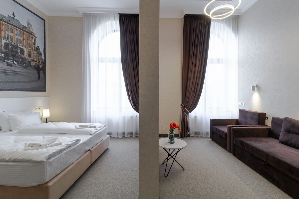 A hotel room with a bed, a sofa, a small table with a vase of flowers, and a painting on the wall.