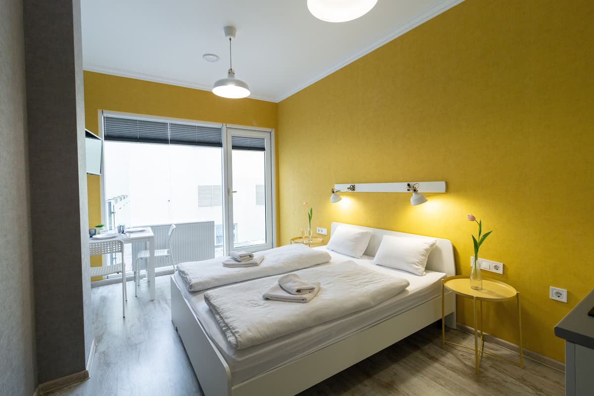 A hotel room with two beds, a small table with a vase of flowers, and a view of the outside balcony.