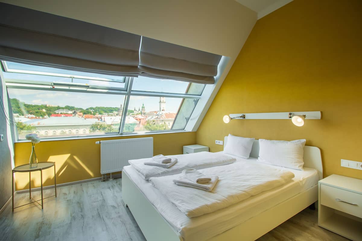 A bedroom with a large window, a bed, a bedside table, and a nightstand.