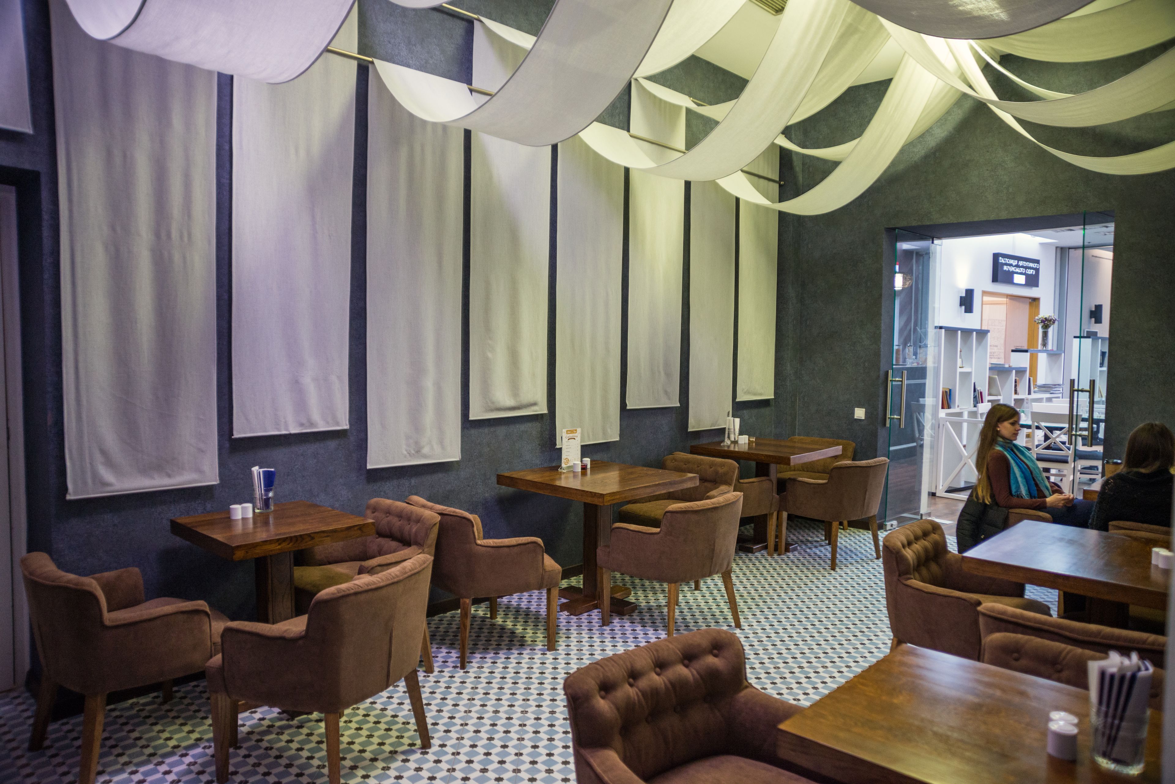A restaurant with wooden tables and chairs, a patterned floor, and hanging fabric.