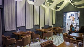 A restaurant with wooden tables and chairs, a patterned floor, and hanging fabric.