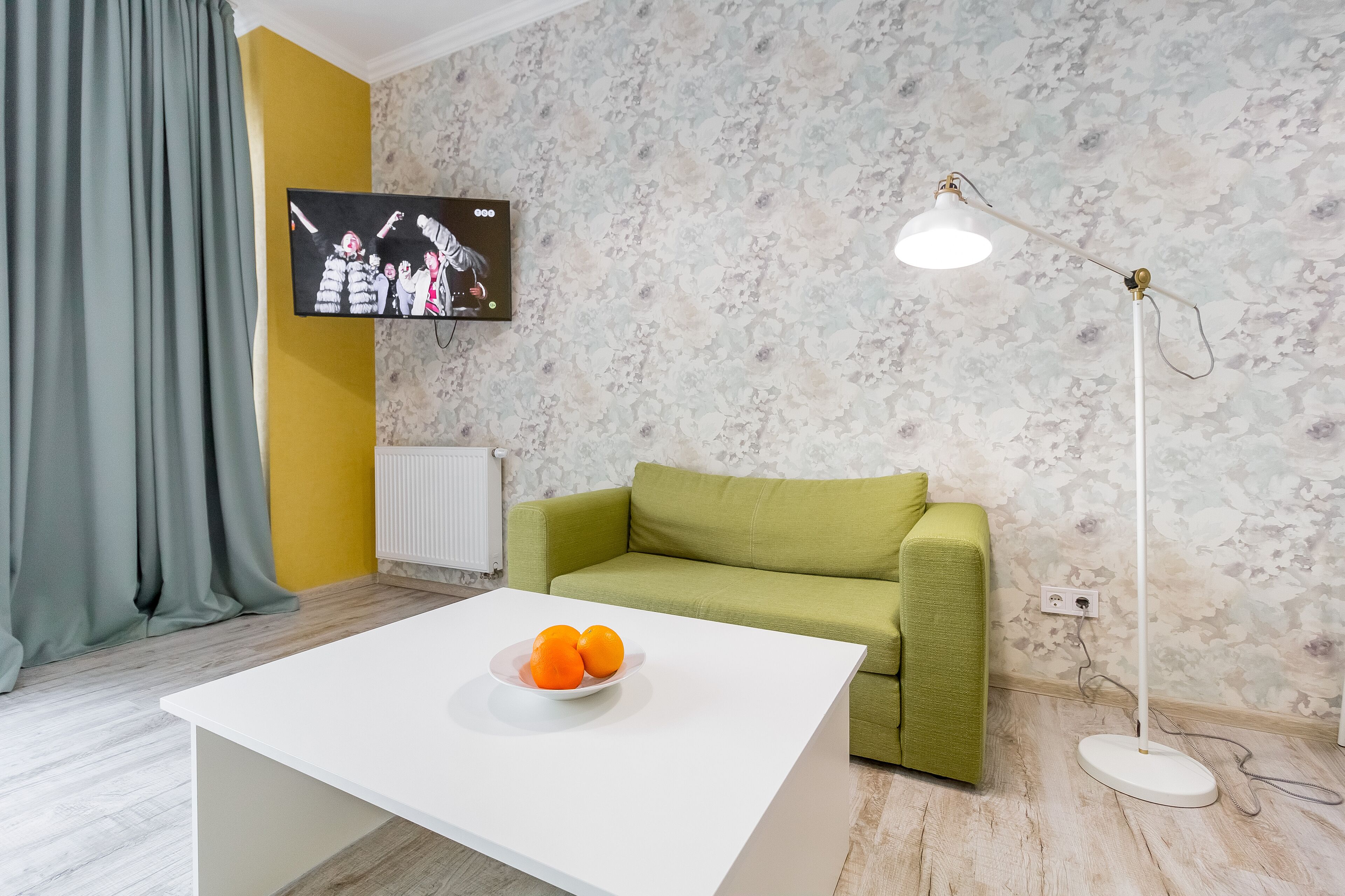 A modern living room with a white coffee table, green sofa, and a flat-screen TV mounted on the wall.