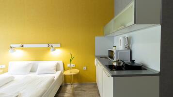 A compact hotel room with a bed, bedside table, and a small kitchenette.