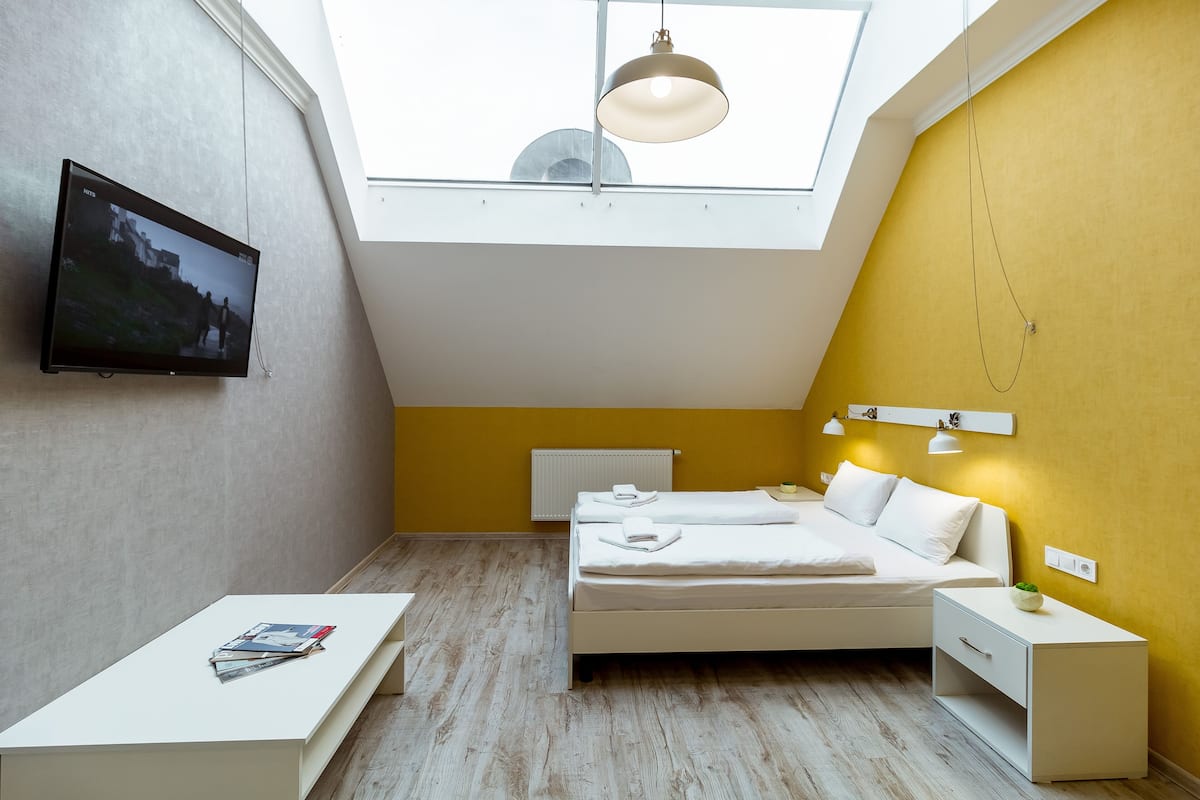 A modern bedroom with a skylight, a bed, bedside tables, and a television on the wall.