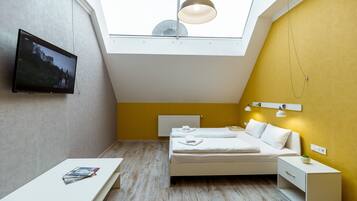 Quarto moderno com claraboia, uma cama, mesas de cabeceira e televisão na parede.