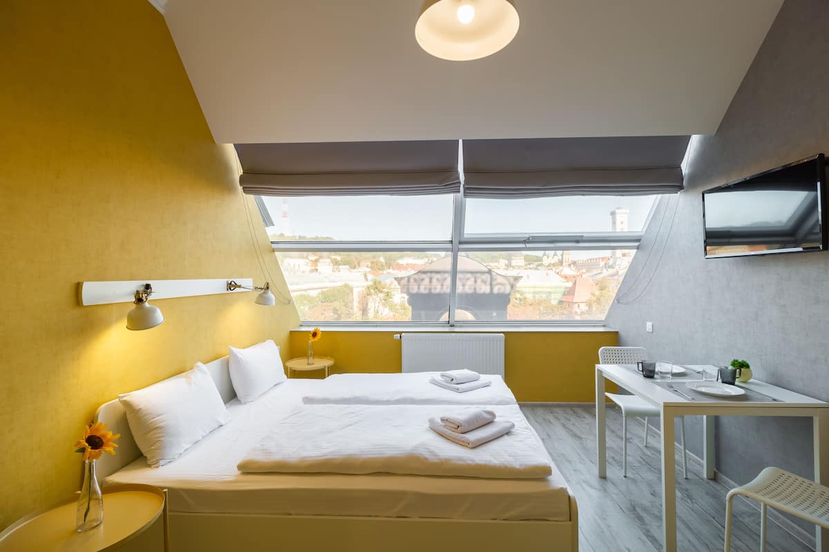 A modern hotel room with a large bed, a desk, and a view of the city.