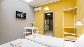 A modern hotel room with a bed, a desk, chairs, a TV, and a bathroom visible through an open door.